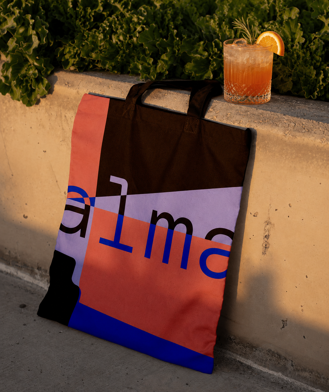 ALMA tote bag leaning against a wall with a cocktail